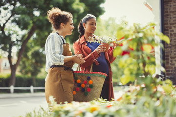 Female florist helping pregnant shopper potted plants at flower shop storefront
