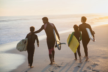 Family surfers walking with surfboards on sunny summer sunset beach