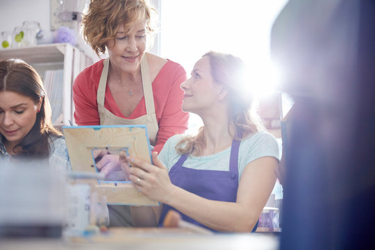 Female instructor helping student painting picture frame in art class workshop