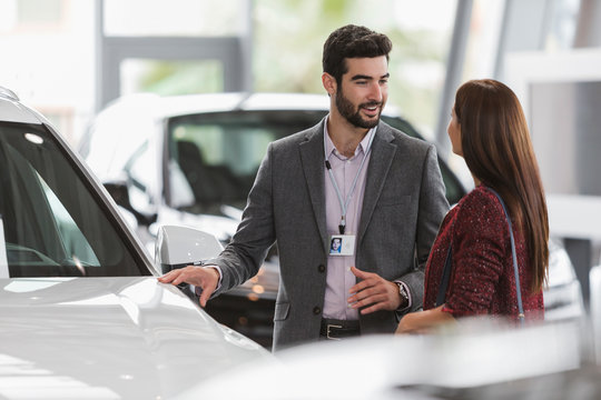 Car salesman showing new car to female customer in car dealership showroom