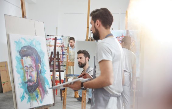 Male artists painting at easel in art class studio