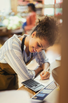 Smiling female cashier using calculator at store counter