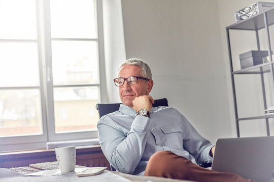 Confident, pensive businessman with laptop looking away in office