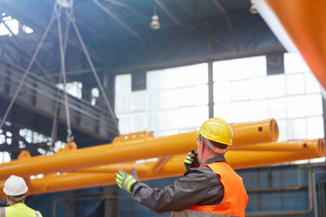 Male worker walkie-talkie guiding lowering of equipment in factory