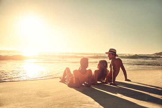 Young friends relaxing on idyllic, sunny summer sunset ocean beach