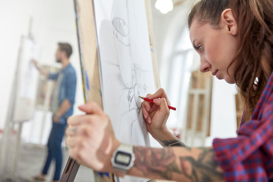 Focused female artist tattoo sketching at easel in art class studio