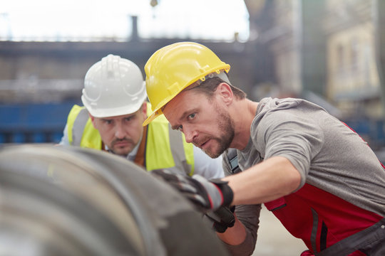 Focused male engineers examining steel part in factory