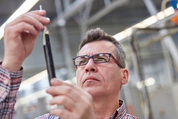 Focused male supervisor examining fiber optic cable in factory