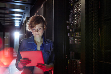Focused female IT technician using digital tablet in server room