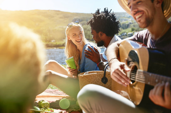 Young friends playing guitar and enjoying sunny summer picnic