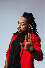 Closeup studio portrait of a man wearing a red jacket suit and dreadlocks. saying stop