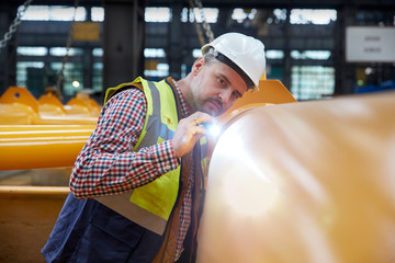 Focused male engineer with flashlight examining equipment in factory