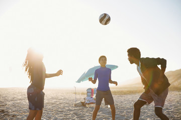 Family playing soccer on sunny summer beach