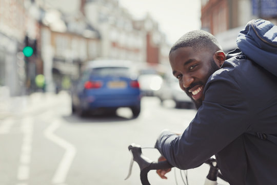 Smiling young businessman commuting, riding bicycle on sunny urban street