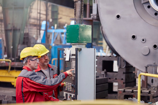 Male workers operating machinery at control panel in factory