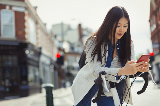 Young woman commuting on bicycle, texting cell phone on sunny urban street