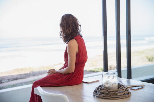 Pensive, serene brunette woman looking at ocean view from dining room table