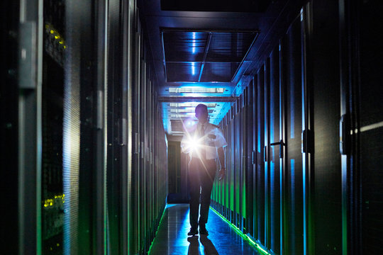 Male security guard with flashlight walking in dark server room