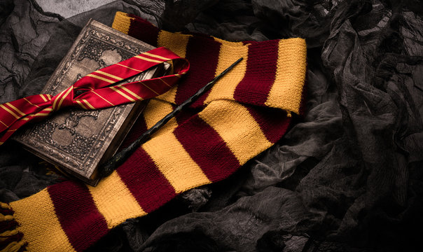Subjects of the school of magic. Scarf, magic wand, book of spells on grey dark rag background.
