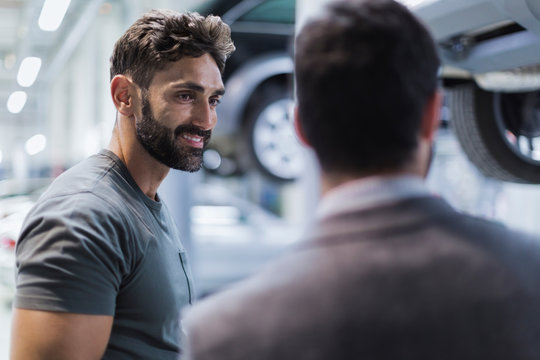 Smiling male auto mechanic talking to customer in auto repair shop