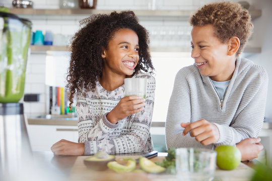 Smiling brother and sister drinking healthy green smoothie in kitchen