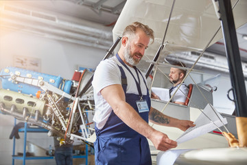 Male mechanical engineer reviewing plans at airplane in hangar
