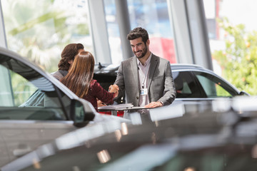 Car salesman handshaking with customers in car dealership showroom