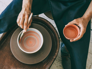 Ceramist at a pottery workshop Top view photo Man is glazing a ceramic plate at rotating potter's wheel - obrazy, fototapety, plakaty