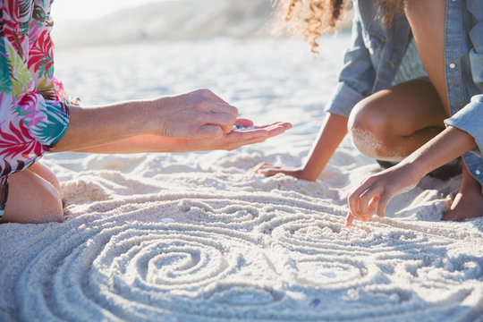 Mother daughter placing seashells in spirals in son sunny summer beach