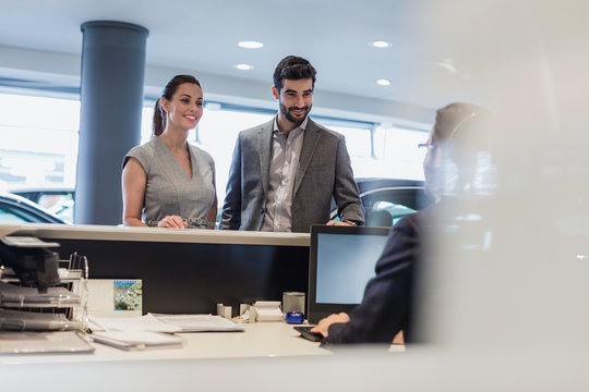 Couple at reception desk in car dealership showroom