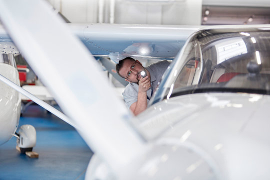Mechanic engineer examining underside of airplane wing flashlight in hangar