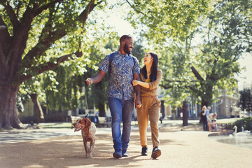 Happy young couple walking dog in sunny park