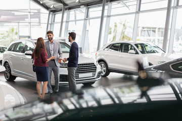 Car salesman talking to couple customers in car dealership showroom