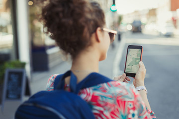 Young female tourist backpack using GPS on smart phone on urban street