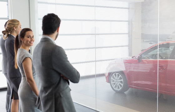 Car sales people looking at new, red car in car dealership showroom
