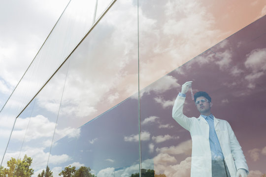 Scientist examining liquid in beaker at modern window cloud reflections
