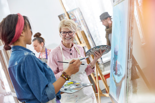 Smiling female artists paintbrushes palettes painting in art class studio