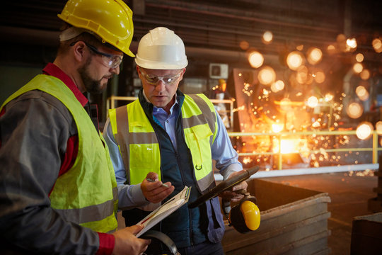 Supervisor and steelworker with clipboard talking in steel mill