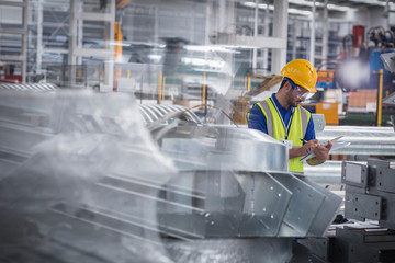 Factory worker with clipboard inspecting steel parts in factory