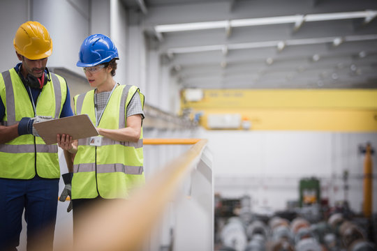 Supervisors with clipboard talking on platform in factory