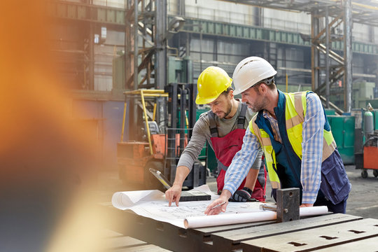 Male engineers reviewing blueprints in factory