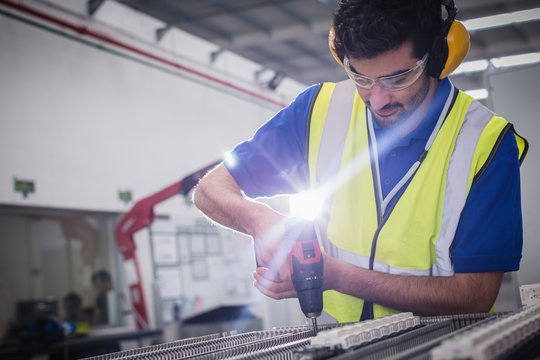 Male engineer with power drill assembling equipment in steel factory