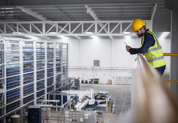 Male supervisor with clipboard on platform looking down at factory