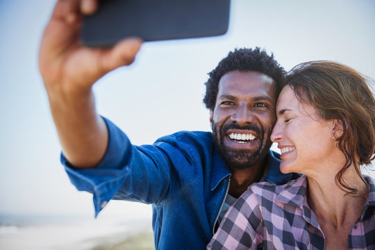 Affectionate, happy multi-ethnic couple taking selfie camera phone