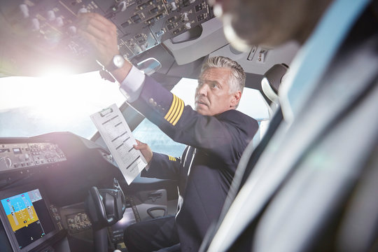 Male pilot clipboard preparing, adjusting instruments in airplane cockpit