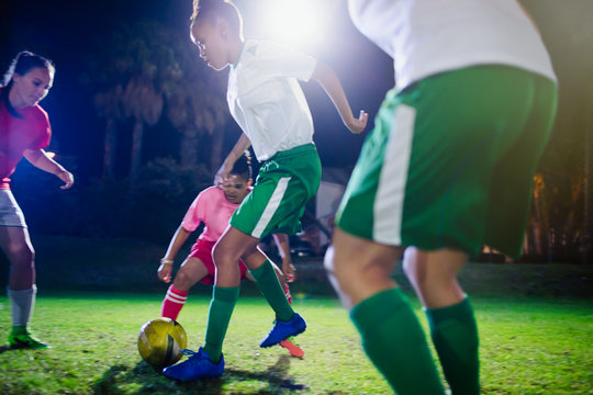Young female soccer players playing on field at night