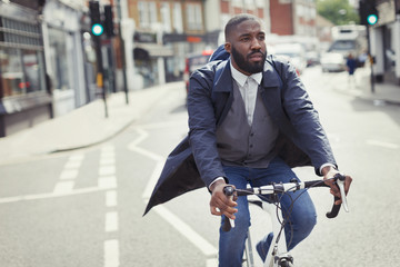 Young male businessman commuting on bicycle on sunny urban street