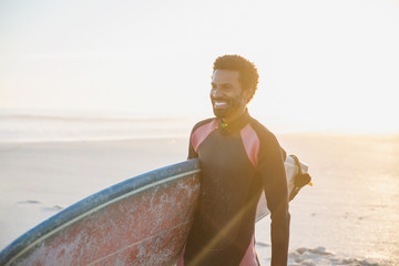 Smiling male surfer walking with surfboard on sunny summer beach