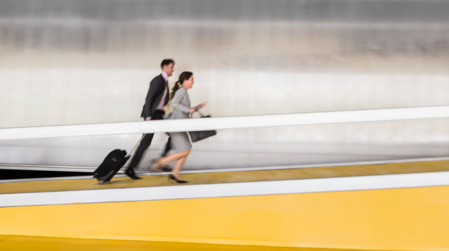 Businessman and businesswoman with suitcase running up airport ramp