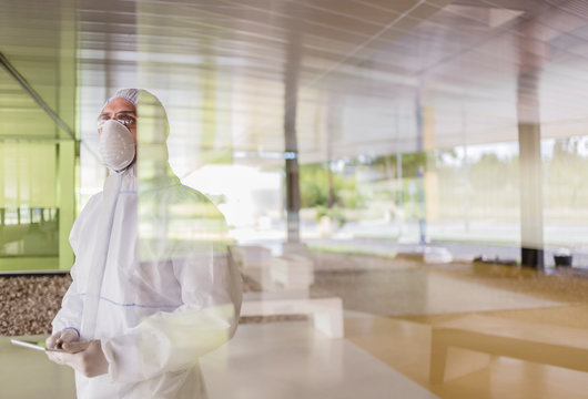 Scientist in clean suit using digital tablet at window